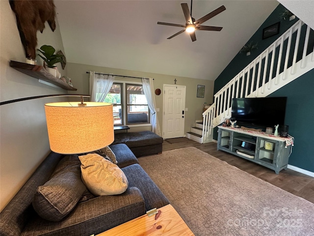 living area with baseboards, ceiling fan, stairway, dark wood-type flooring, and vaulted ceiling