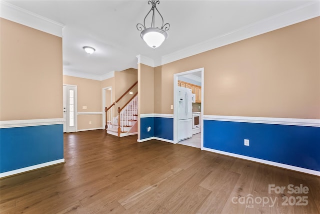 spare room with stairs, baseboards, ornamental molding, and wood finished floors