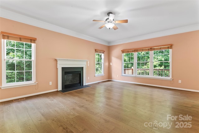 unfurnished living room featuring crown molding, a glass covered fireplace, a ceiling fan, baseboards, and visible vents