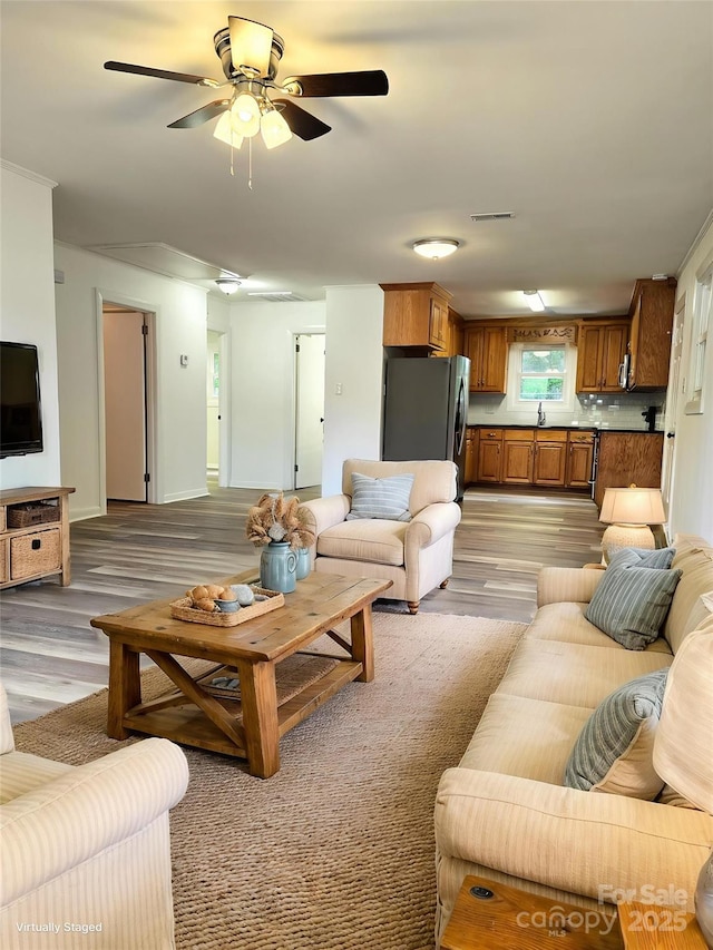 living room featuring a ceiling fan, baseboards, visible vents, and light wood finished floors