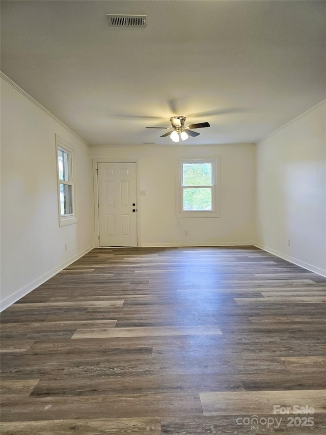 empty room featuring visible vents, ornamental molding, dark wood-style flooring, baseboards, and a ceiling fan