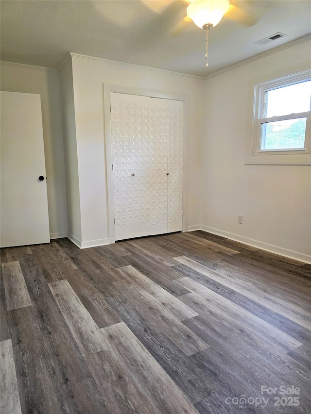 unfurnished bedroom featuring visible vents, ornamental molding, a closet, wood finished floors, and baseboards
