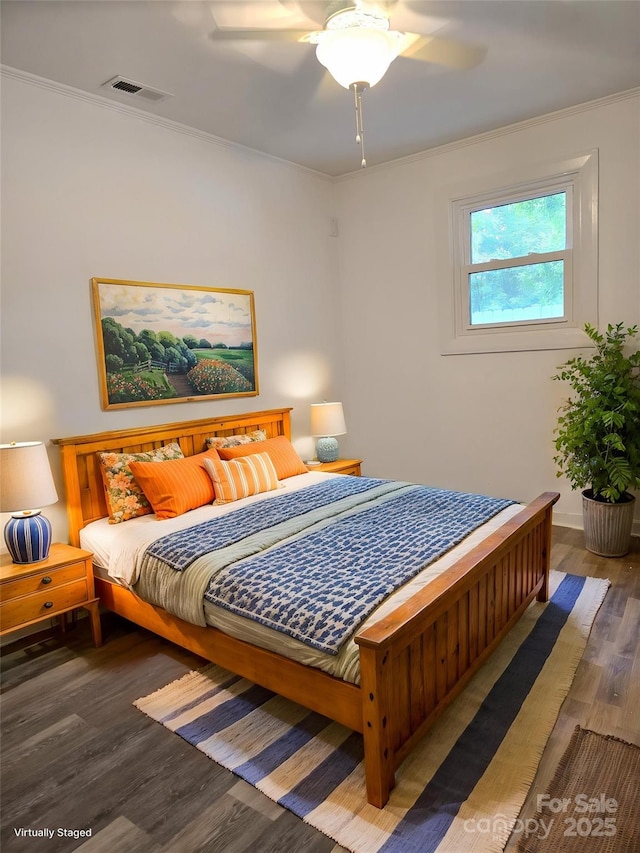 bedroom featuring ceiling fan, visible vents, wood finished floors, baseboards, and ornamental molding