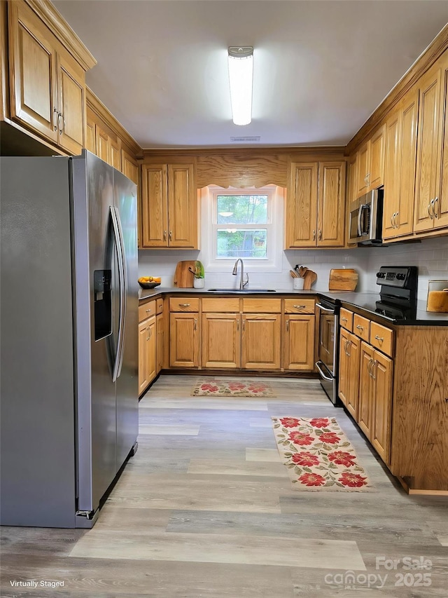 kitchen with stainless steel appliances, dark countertops, a sink, and light wood-type flooring