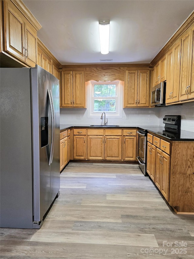kitchen with dark countertops, brown cabinets, a sink, light wood-style floors, and stainless steel appliances