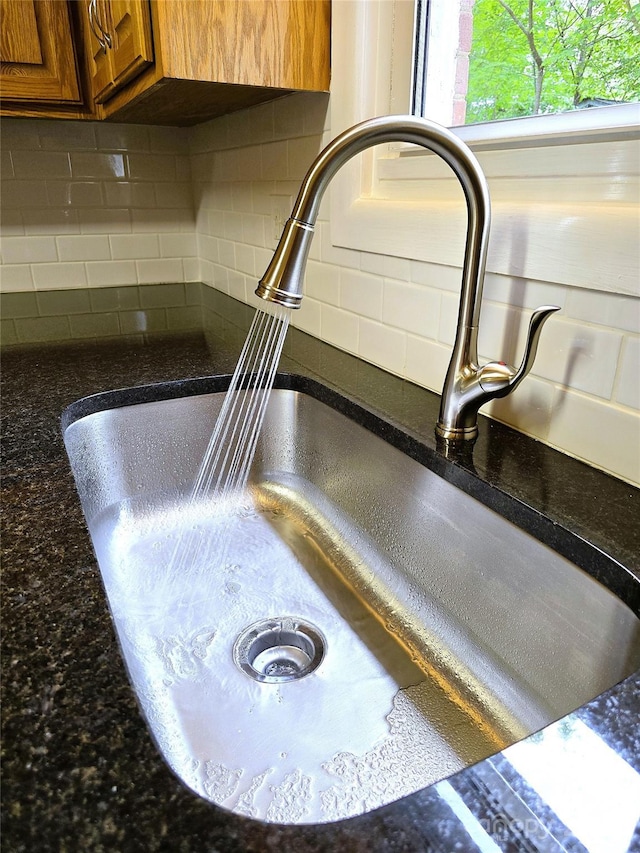 details featuring decorative backsplash, brown cabinetry, a sink, and dark stone countertops