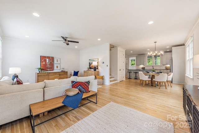 living room featuring recessed lighting, light wood finished floors, and ceiling fan with notable chandelier