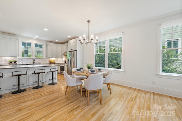 dining space with baseboards, light wood finished floors, a notable chandelier, and a wealth of natural light