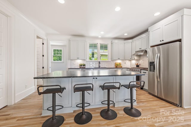 kitchen with a center island, a kitchen breakfast bar, stainless steel appliances, and under cabinet range hood