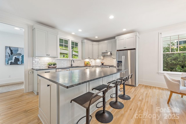 kitchen featuring dark countertops, appliances with stainless steel finishes, a breakfast bar area, baseboards, and under cabinet range hood