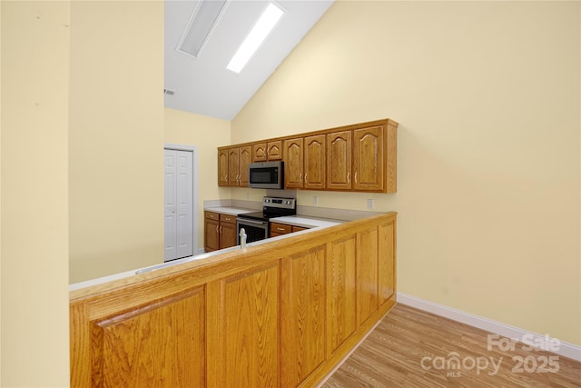 kitchen with brown cabinetry, light countertops, high vaulted ceiling, light wood finished floors, and stainless steel appliances