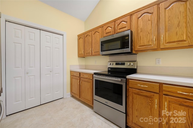 kitchen with brown cabinetry, light countertops, vaulted ceiling, and stainless steel appliances