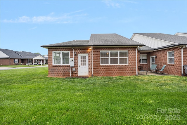 back of property with a patio, a shingled roof, a yard, and brick siding