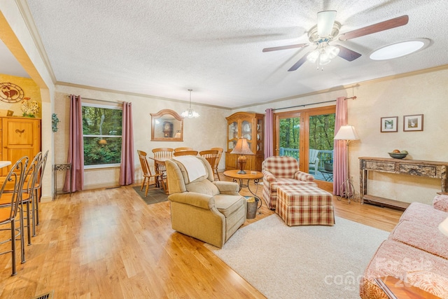 living room with a textured ceiling, ornamental molding, wood finished floors, a ceiling fan, and a chandelier