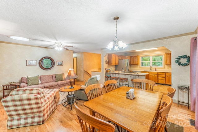 dining room featuring a textured ceiling, crown molding, light wood-style flooring, ceiling fan, and a chandelier