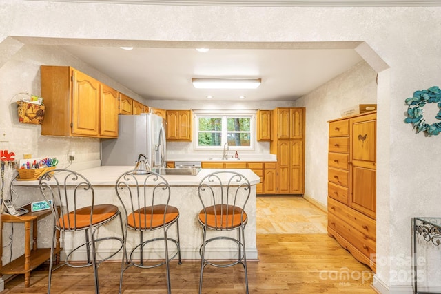 kitchen with a sink, a peninsula, stainless steel refrigerator with ice dispenser, light countertops, and a breakfast bar