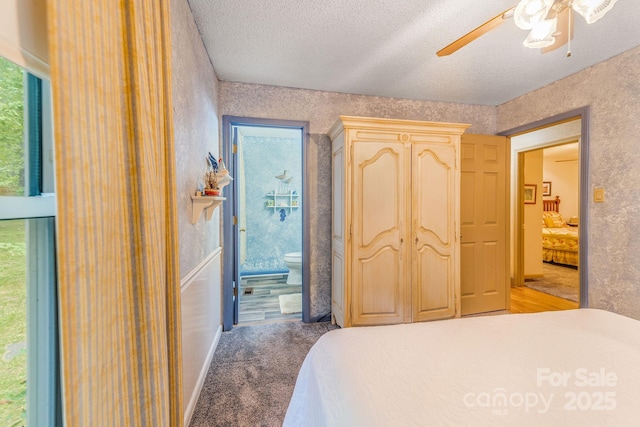 bedroom featuring a textured ceiling, ensuite bathroom, multiple windows, light carpet, and a ceiling fan