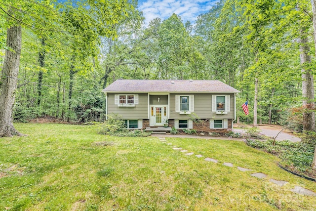 raised ranch with a front lawn, brick siding, entry steps, and a view of trees