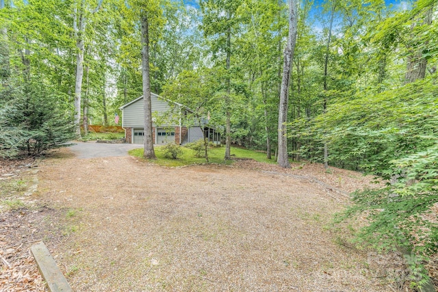 view of yard with asphalt driveway and a view of trees