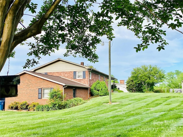 view of side of home featuring a lawn, a chimney, and brick siding
