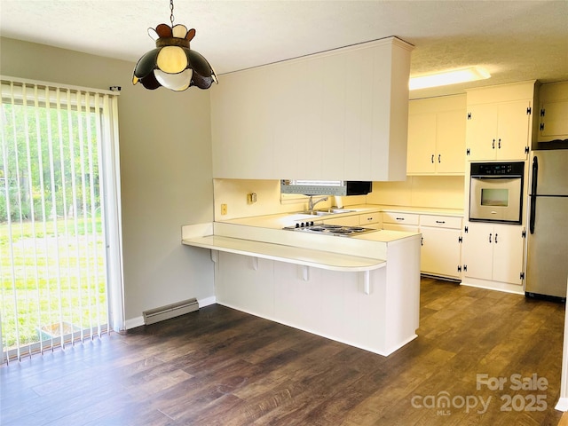kitchen featuring dark wood-style flooring, appliances with stainless steel finishes, light countertops, a sink, and a peninsula