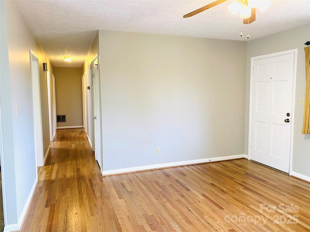 empty room with ceiling fan, a textured ceiling, visible vents, baseboards, and light wood finished floors
