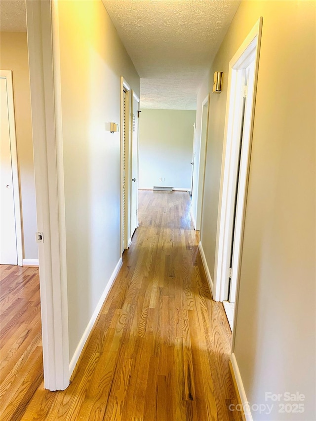 hall with a textured ceiling, baseboards, and wood finished floors