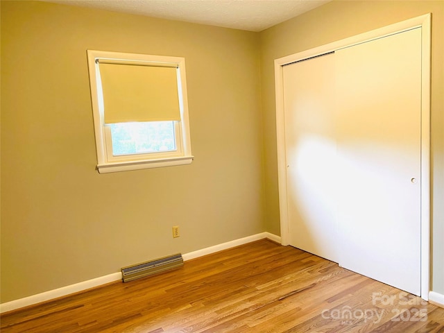 unfurnished bedroom with baseboards, a closet, wood finished floors, and visible vents