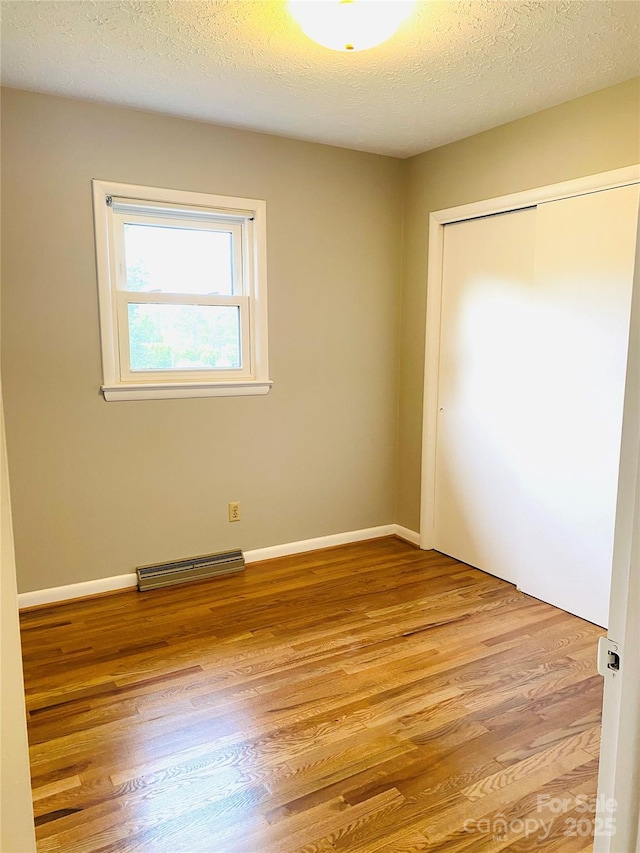 unfurnished bedroom featuring a textured ceiling, visible vents, baseboards, a closet, and light wood-style flooring