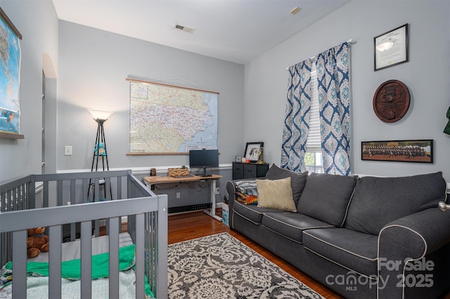 bedroom with visible vents, a crib, and wood finished floors