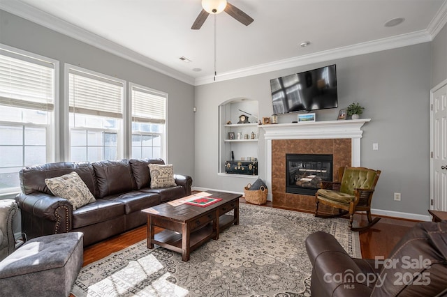 living room with ornamental molding, built in features, wood finished floors, ceiling fan, and a tiled fireplace