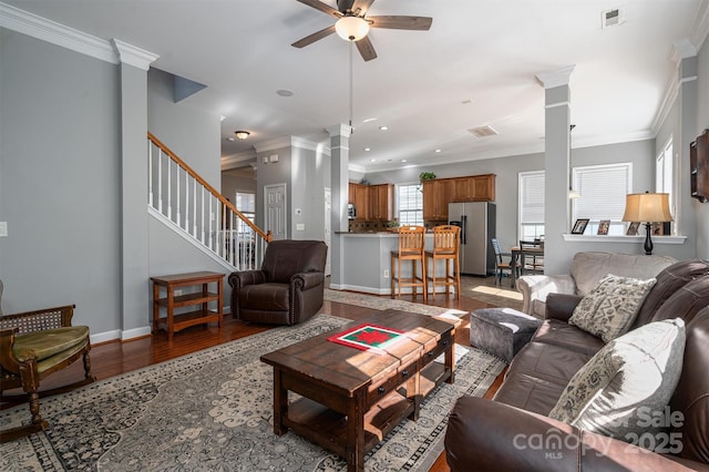 living area featuring ceiling fan, ornamental molding, decorative columns, and visible vents