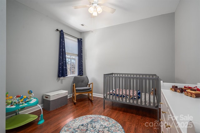 bedroom featuring visible vents, wood finished floors, baseboards, ceiling fan, and a crib