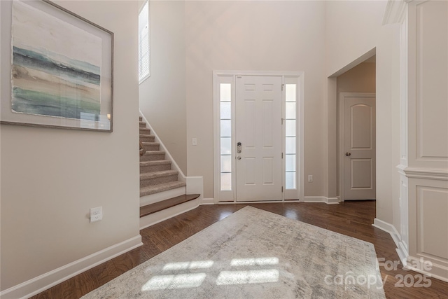 entrance foyer featuring a healthy amount of sunlight, a towering ceiling, dark wood finished floors, stairway, and baseboards