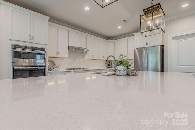 kitchen with light stone countertops, under cabinet range hood, tasteful backsplash, a sink, and appliances with stainless steel finishes