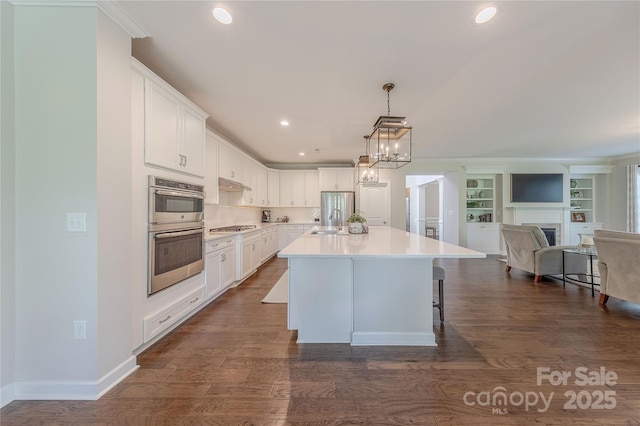 kitchen featuring a kitchen island with sink, open floor plan, white cabinets, a sink, and stainless steel appliances