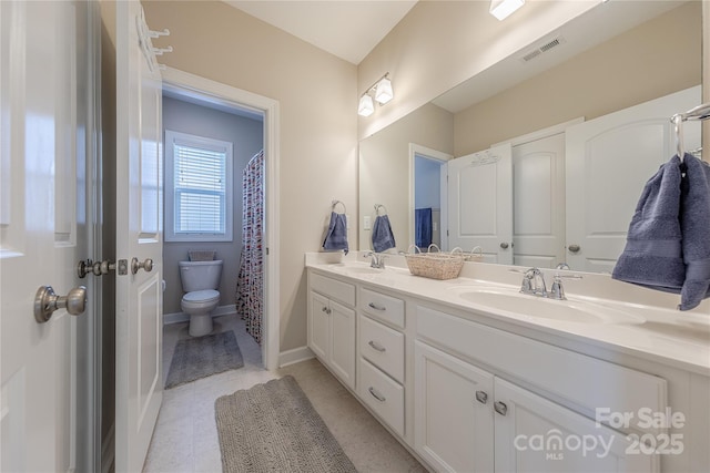 bathroom featuring baseboards, double vanity, toilet, and a sink