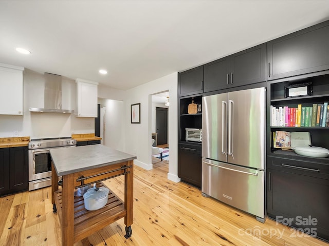 kitchen featuring wall chimney range hood, open shelves, light wood finished floors, light countertops, and stainless steel appliances