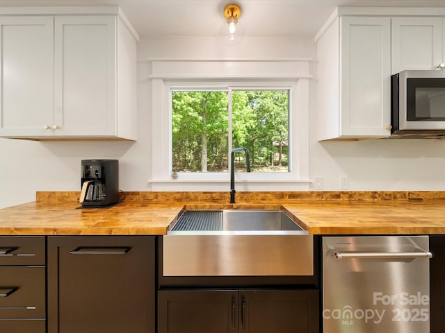 kitchen with a sink, appliances with stainless steel finishes, white cabinets, and wooden counters
