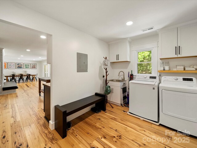 clothes washing area featuring electric panel, independent washer and dryer, visible vents, a sink, and light wood-style floors