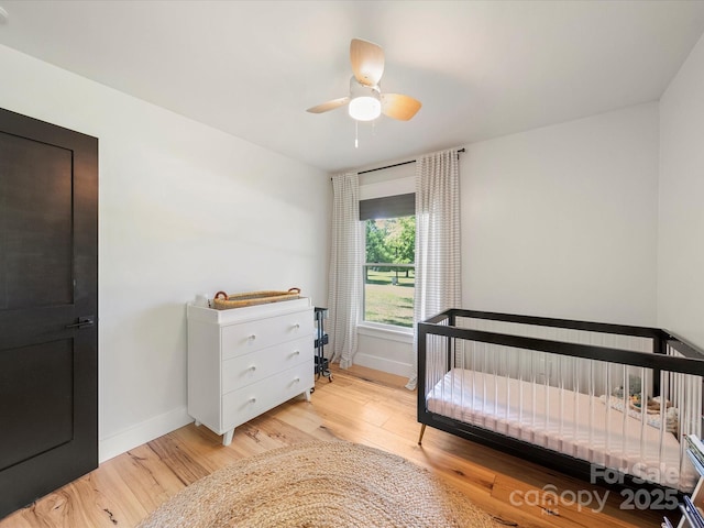 bedroom with baseboards, light wood finished floors, ceiling fan, and a nursery area