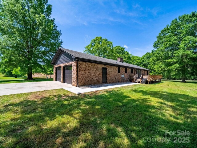 view of side of property with a wooden deck, a chimney, brick siding, a lawn, and driveway