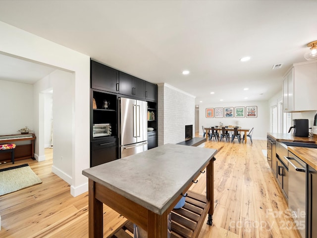 1207 Carlson Dr, Monroe, NC 28110 - kitchen with appliances with stainless steel finishes, light wood finished floors, a fireplace, recessed lighting, and dark cabinetry