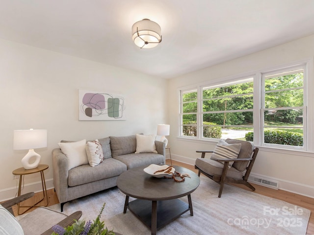 living area with baseboards, light wood-style flooring, and visible vents