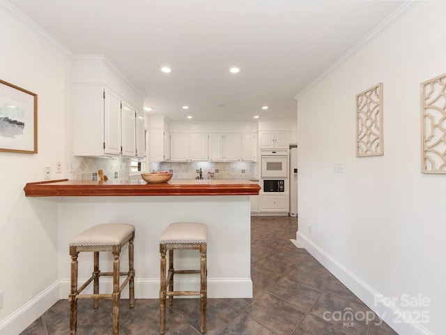 kitchen with decorative backsplash, a breakfast bar area, baseboards, white cabinets, and a peninsula