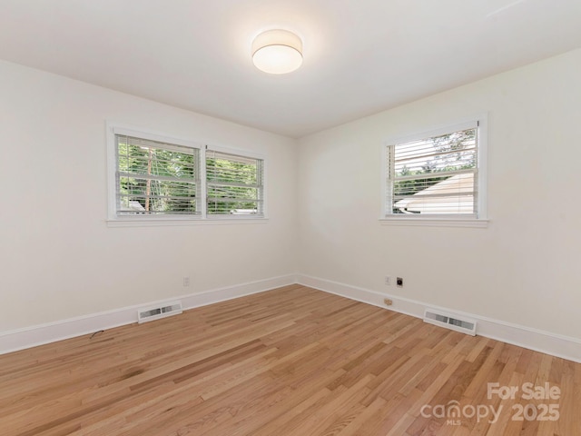 empty room with visible vents, a wealth of natural light, and light wood-type flooring