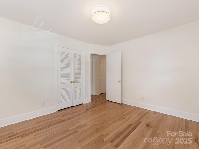 unfurnished bedroom with a closet, baseboards, and light wood-type flooring