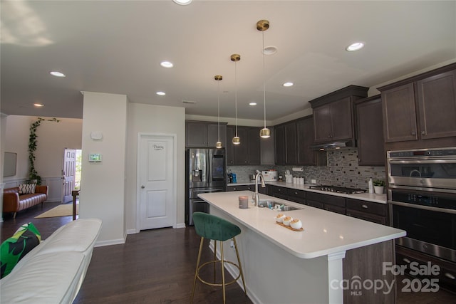 kitchen with a sink, light countertops, stainless steel appliances, tasteful backsplash, and a center island with sink