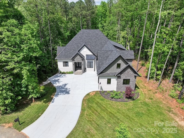 view of front of house featuring a shingled roof, stone siding, board and batten siding, a front yard, and concrete driveway