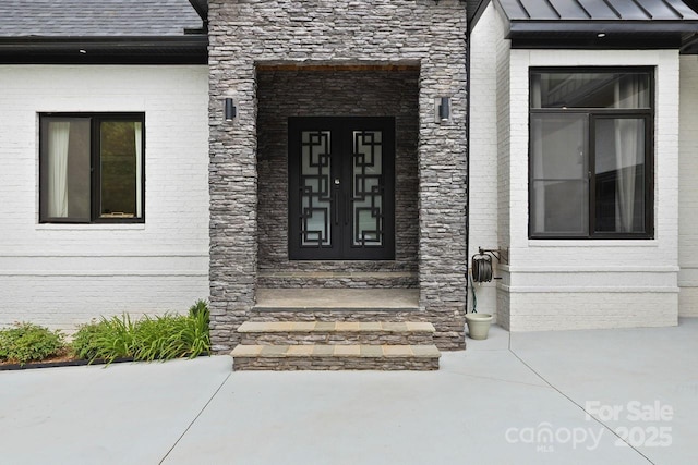 entrance to property featuring brick siding, stone siding, and a standing seam roof